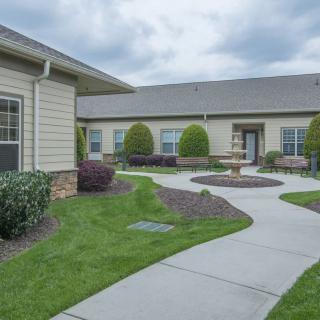 A well-maintained courtyard with a walkway winding through neatly landscaped shrubs and grass, surrounded by buildings under an overcast sky.