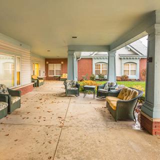 A covered patio area with outdoor seating and a pathway, adjacent to a building.