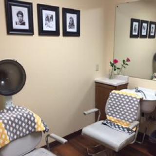 A cozy hair salon interior with styling chairs, a wall-mounted mirror, and framed photos.