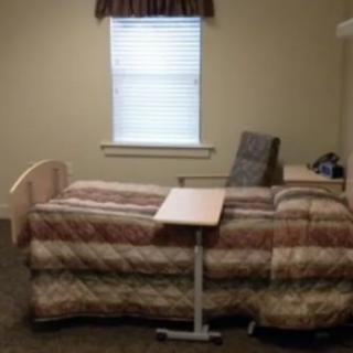 A simple room with a hospital bed, side table, and chair by the window.