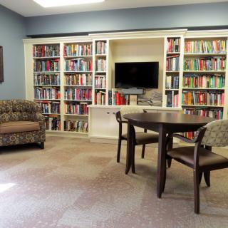 A cozy library room with bookshelves, a table, chairs, and a sofa.