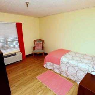 A minimalist bedroom with a single bed, wooden flooring, and simple furnishings.