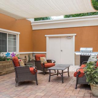 A cozy patio with rattan seating, a central table, and a grill under a shaded canopy.
