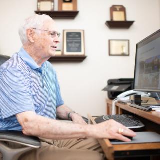 An elderly person working on a computer in an office setting.