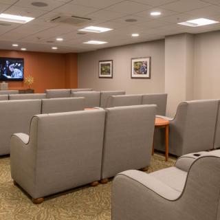 A waiting room with rows of gray chairs facing a television on the wall.