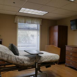 A comfortable and well-lit hospital room featuring a patient bed, window with curtains, and basic furnishings.