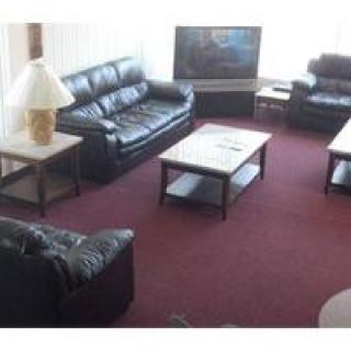 A living room with leather sofas, a coffee table, a lamp, and a television on a red carpet.