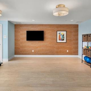 A modern living room with wood paneling, featuring a mounted TV and artwork on the wall, alongside a shelf with exercise equipment.