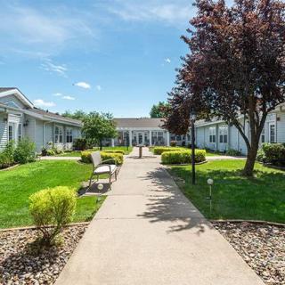 A sunny day at a landscaped outdoor area with a concrete pathway, surrounded by greenery and buildings.