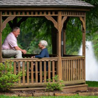 A man and woman talking in a gazebo by a fountain in a park.