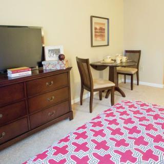 A cozy bedroom with a TV on a dresser, a small table and chairs, and a bed with a patterned bedspread.