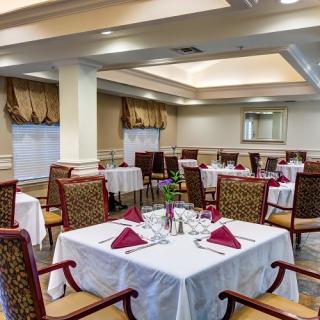 A well-lit dining room with neatly arranged tables and chairs, featuring elegant table settings with red napkins.