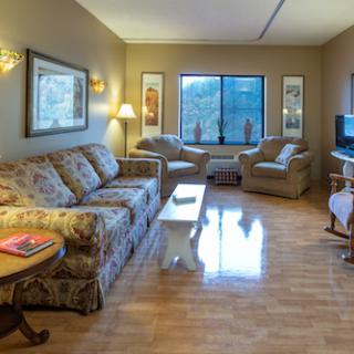 A cozy living room with floral patterned furniture and warm lighting, featuring a view through a large window.