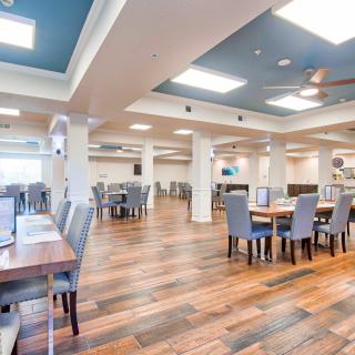 A spacious and modern dining area featuring wooden floors, multiple tables, and cushioned chairs.