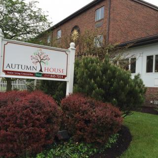 A brick building with a sign reading 'Autumn House' surrounded by well-maintained bushes and trees.