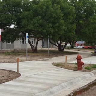 A newly constructed sidewalk curves around trees, with a fire hydrant visible in the foreground.