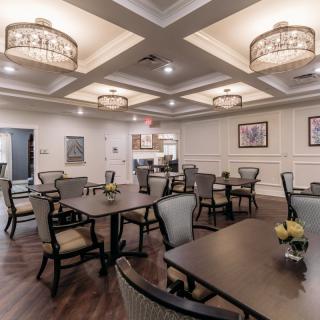 An elegant dining room with neatly arranged tables and chairs, featuring decorative lighting and a coffered ceiling.