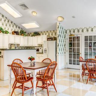 A spacious kitchen with a dining area featuring wooden chairs and tables, bright cabinets, and patterned wallpaper.