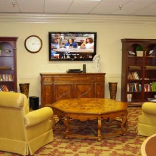 A cozy living room with armchairs, a coffee table, bookshelves, and a wall-mounted television.