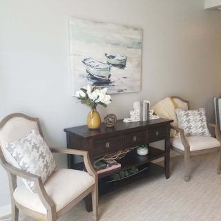 A cozy living room corner featuring elegant chairs, a dark wooden console table, and a nautical-themed painting on the wall.