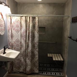 A bathroom featuring a shower with a floral curtain, a small wall-mounted sink, and a decorative tiled floor with a step stool.