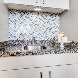 Modern kitchen sink with granite countertop and stylish chevron-patterned backsplash.