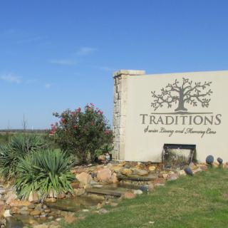 Entrance sign for 'Traditions' with natural landscaping and blue sky.