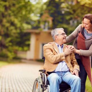 A caregiver assisting a senior man in a wheelchair outdoors.
