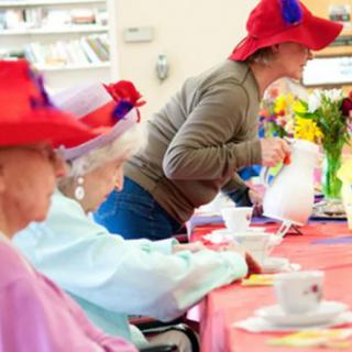 A group of seniors enjoying a tea party, wearing red hats.