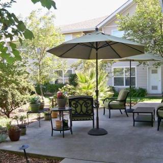 A cozy patio setup with outdoor furniture and an umbrella, surrounded by lush greenery.