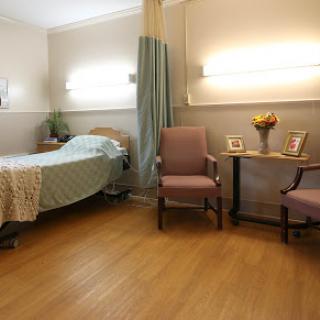 A serene hospital room with a bed, two chairs, decorative flowers, and framed pictures.