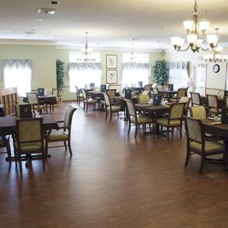 A spacious and well-lit dining room with multiple tables and chairs, featuring chandeliers and a wooden floor.