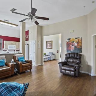 A cozy living room with comfortable seating and a ceiling fan, featuring wood flooring and colorful artwork.