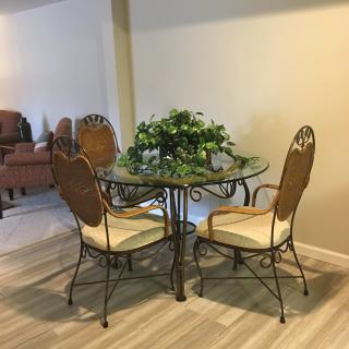 A cozy dining area featuring a glass table with decorative indoor plants and wicker chairs.