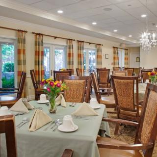 An elegant dining room with neatly arranged tables and chairs, complete with floral centerpieces and soft lighting from chandeliers.