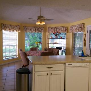 A bright kitchen with yellow walls and a dining area featuring large windows and a ceiling fan.