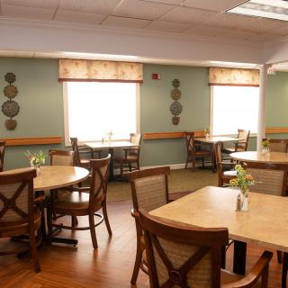 An empty dining room with wooden tables and chairs, decorated with wall ornaments and natural lighting from the windows.
