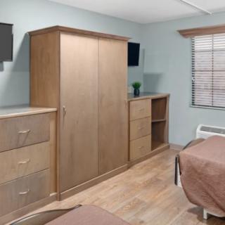 A minimalist bedroom featuring wooden furniture with a wardrobe, dresser, and bed.
