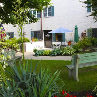 A serene garden with a bench, plants, and patio area outside a building.
