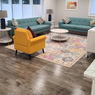 A modern living room with teal sofas, a yellow armchair, a colorful rug, and wood flooring.