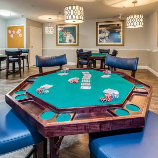 A game room featuring a poker table with cards and chips neatly arranged, surrounded by blue chairs.