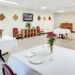 A bright dining room with tables set with white tablecloths and vases of flowers.