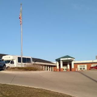 A view of a commercial building with an American flag and parked vehicles.
