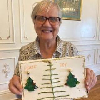 A person smiling and holding a crafted artwork featuring trees.
