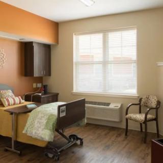 A hospital room with a patient bed and seating area, featuring a window with blinds.