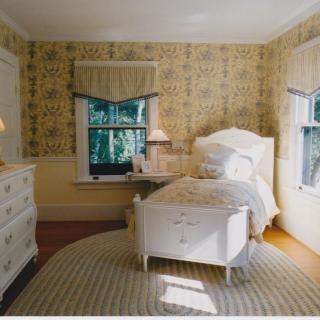 A cozy vintage bedroom with a single bed and decorative wallpaper, illuminated by natural light.
