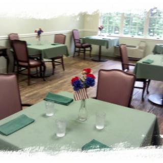 An empty dining room with neatly arranged tables and chairs, featuring vases with flowers as centerpieces.
