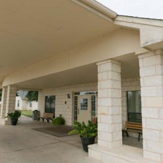 A building entrance with columns and a covered walkway, featuring benches and decorative plants.
