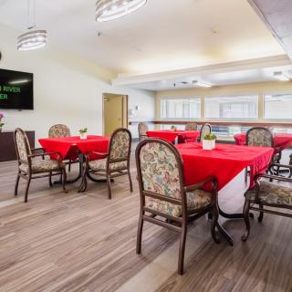 A bright dining area with red tablecloths and patterned chairs on a wooden floor.