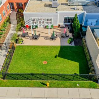 Aerial view of a fenced backyard featuring a green lawn and patio with outdoor seating.